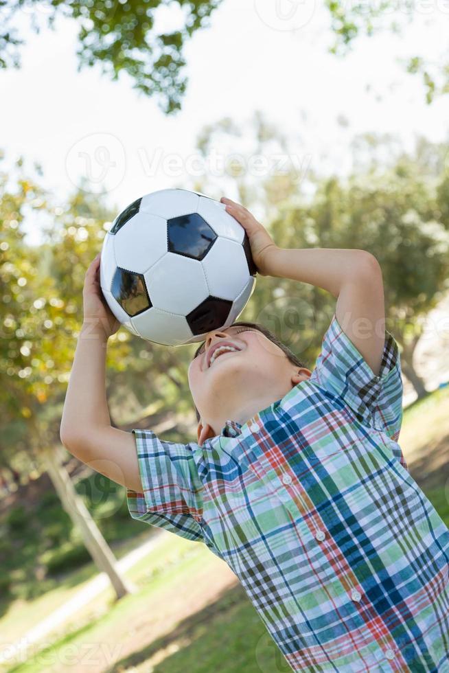 schattige jonge jongen speelt met voetbal buiten in het park. foto