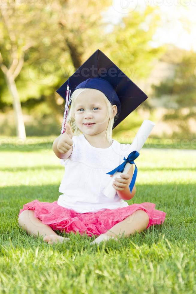 weinig meisje in gras vervelend diploma uitreiking pet Holding diploma met lint foto