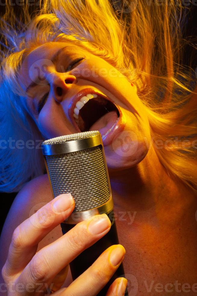 vrouw zanger onder gegeleerde verlichting zingt met passie in condensor microfoon. foto