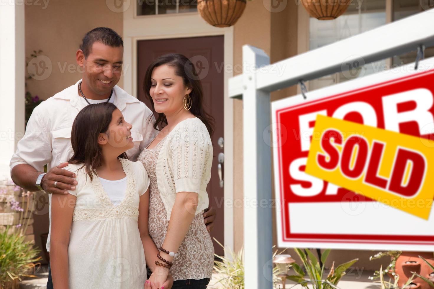 spaans familie in voorkant van hun nieuw huis met verkocht teken foto