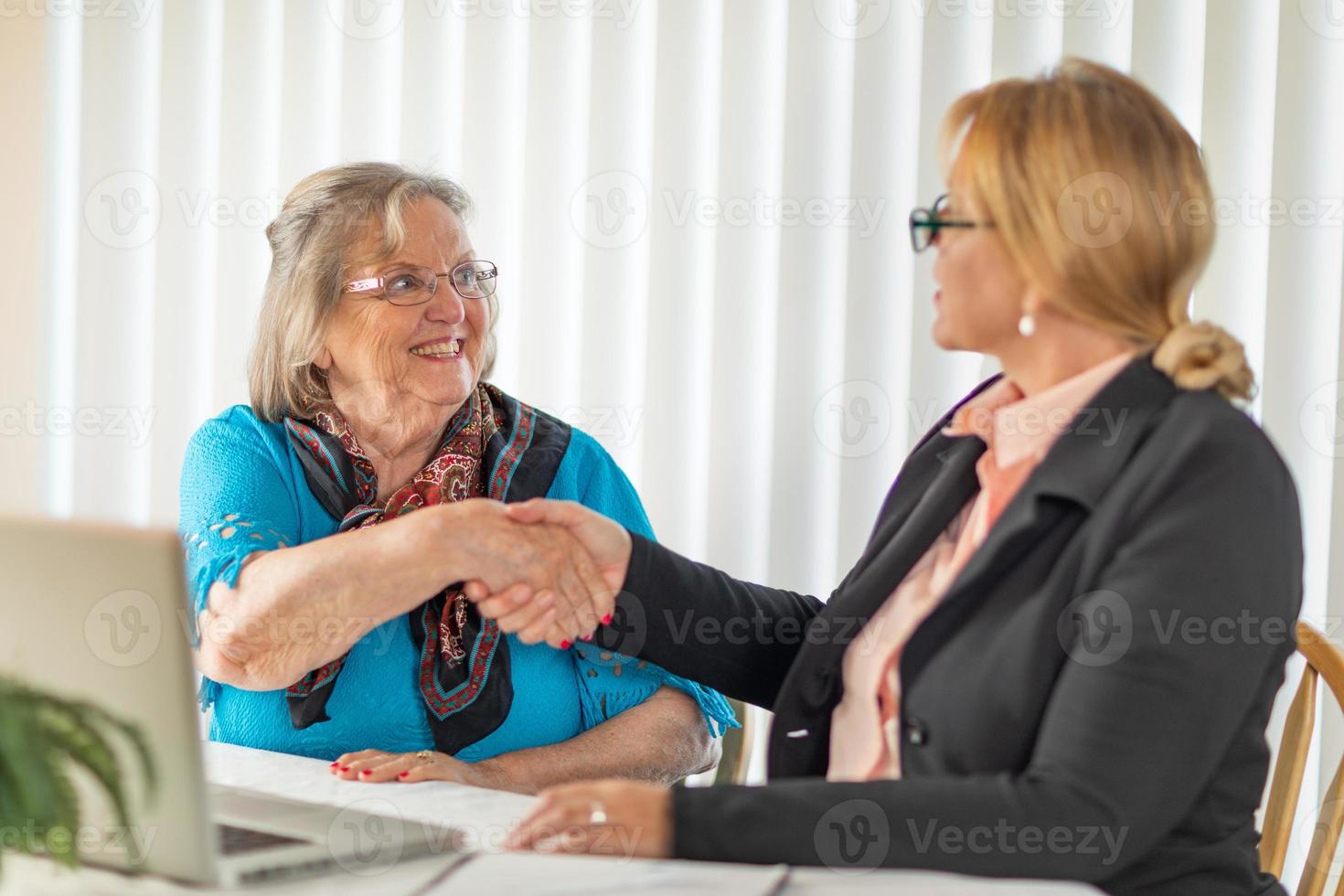 senior vrouw beven handen met zakenvrouw in de buurt laptop computer foto