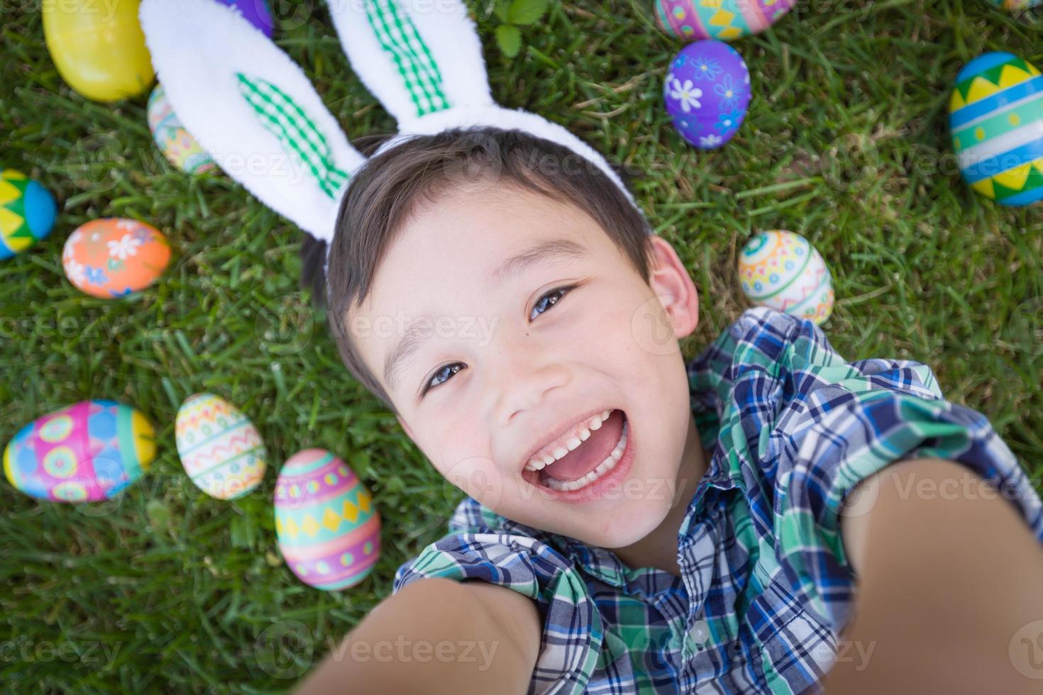 gemengd ras Chinese en Kaukasisch jongen buiten vervelend konijn oren spelen met Pasen eieren foto
