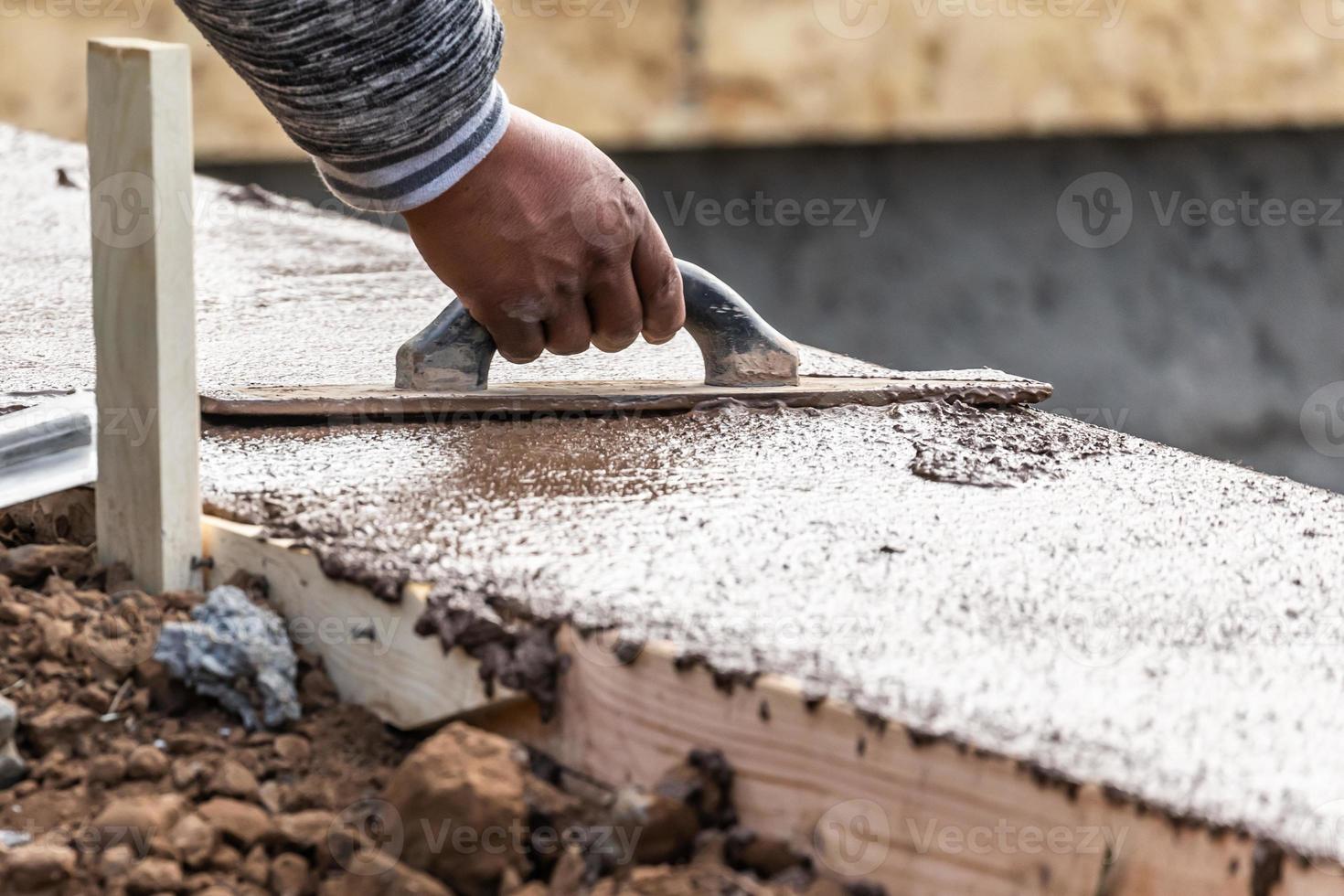 bouw arbeider gebruik makend van hout troffel Aan nat cement vormen omgaan in de omgeving van nieuw zwembad foto