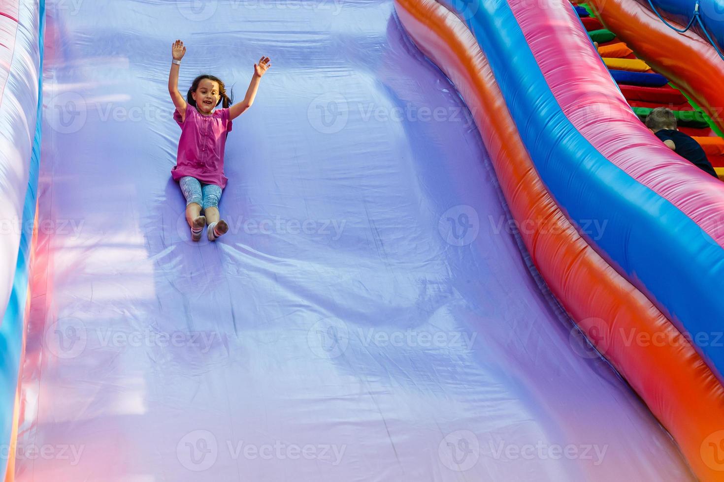 gelukkig weinig meisje hebben veel van pret Aan een jumping kasteel gedurende glijden. foto