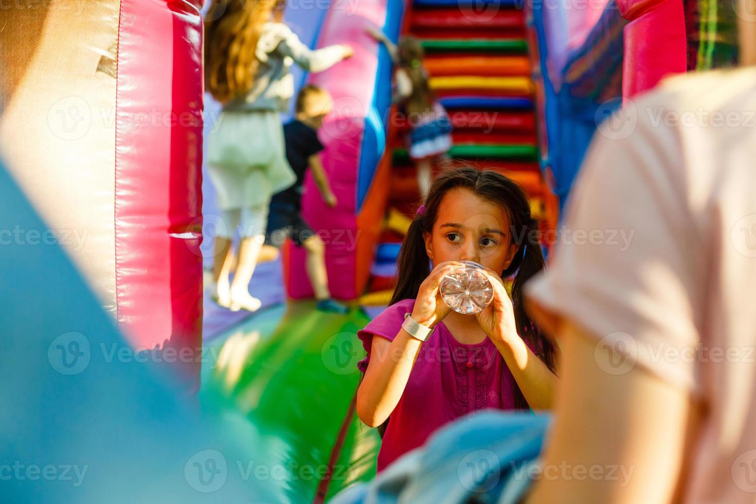 weinig meisje drankjes water Aan een opblaasbaar trampoline foto