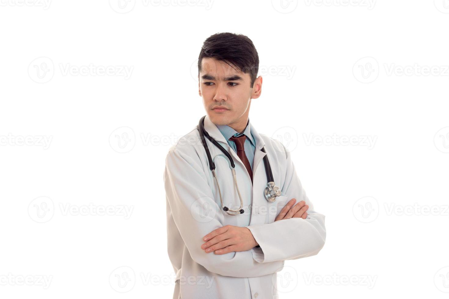 echt brunette mannetje dokter in uniform met stethoscoop Aan zijn nek poseren met gekruiste handen geïsoleerd Aan wit achtergrond foto