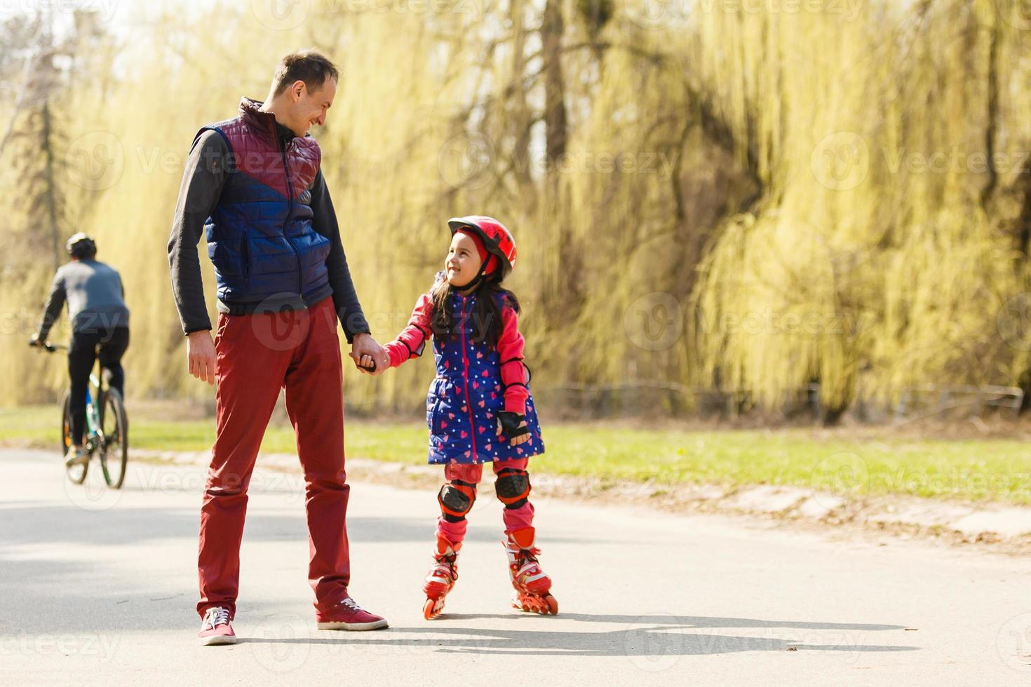 vader onderwijs zijn dochter naar vleet Aan rol schaatsen. gelukkig kind in helm aan het leren het schaatsen. familie uitgeven tijd samen. zonnig zomer dag Aan voorstad straat. foto