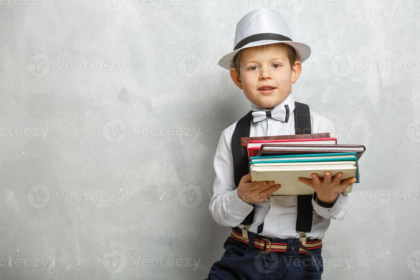 terug naar school. grappig weinig jongen in bril richten omhoog Aan schoolbord. kind van elementair school- met boek en tas. onderwijs. kind met een boek foto