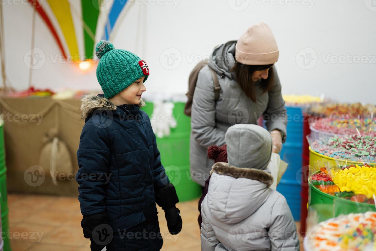 gelukkig weinig kinderen met moeder in een snoep op te slaan kiest snoepgoed, marmelade snoepjes, zet hen in een papier tas. foto