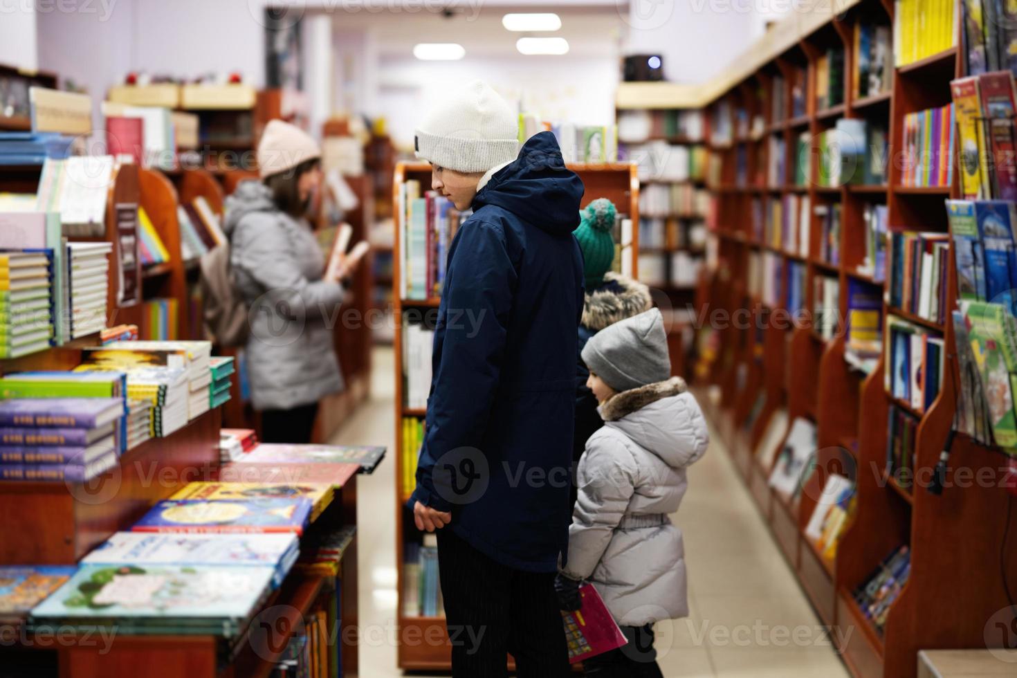 kinderen in jasje bereiken een boek van boekenplank Bij de bibliotheek. aan het leren en onderwijs van Europese kinderen. foto