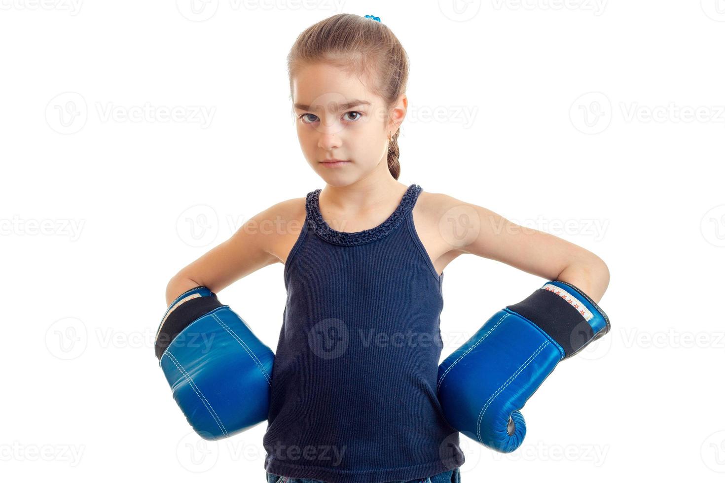 de weinig meisje is staand in een groot volwassen boksen handschoenen en op zoek Bij camera foto