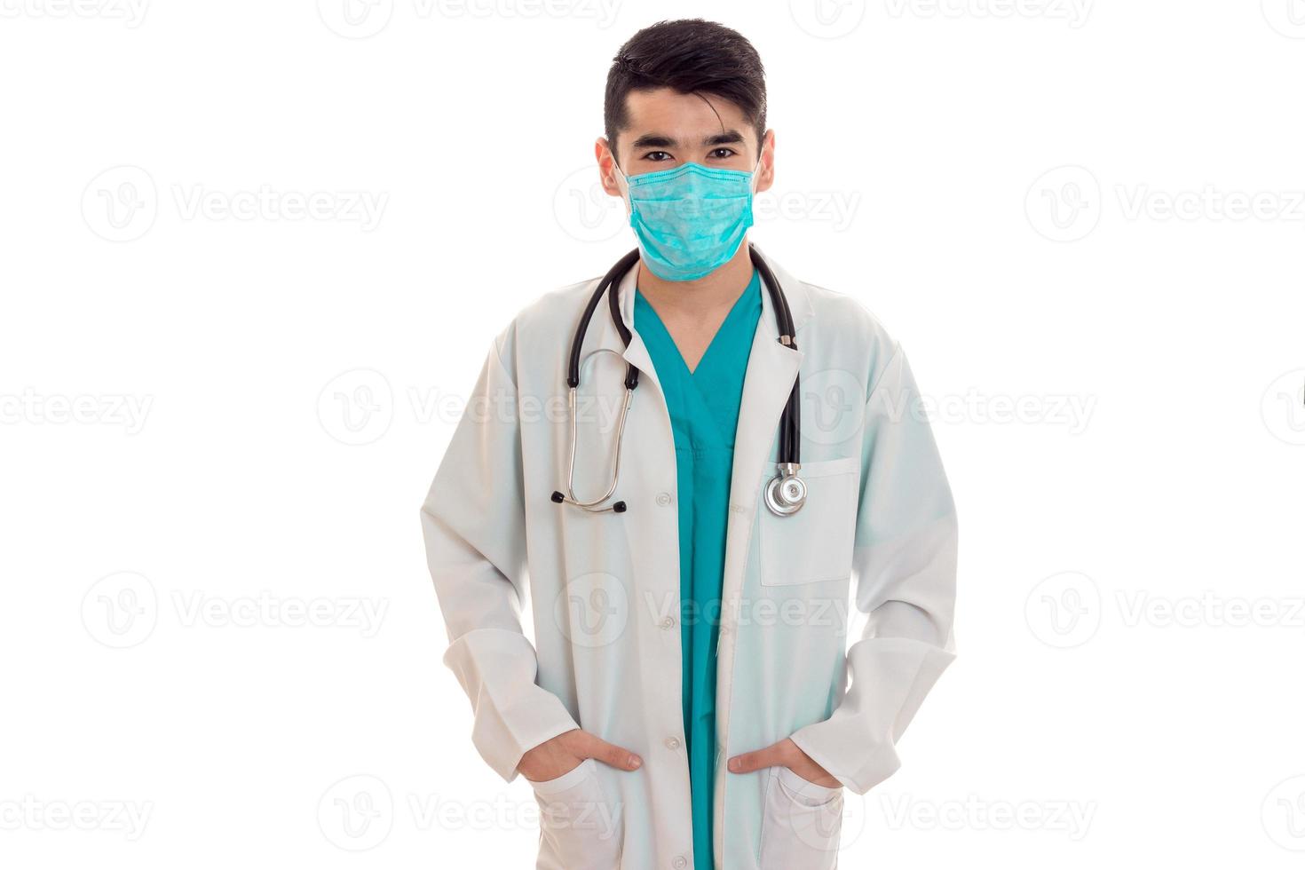 schattig elegant dokter in blauw uniform met stethoscoop en masker poseren en op zoek Bij de camera geïsoleerd Aan wit achtergrond foto