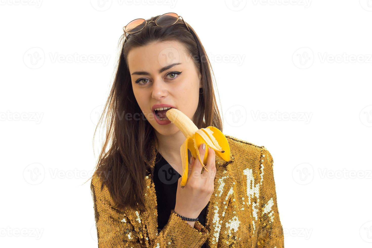 portret van een jong meisje wie staat in de verbazingwekkend studio en houdt banaan in de buurt de mond foto