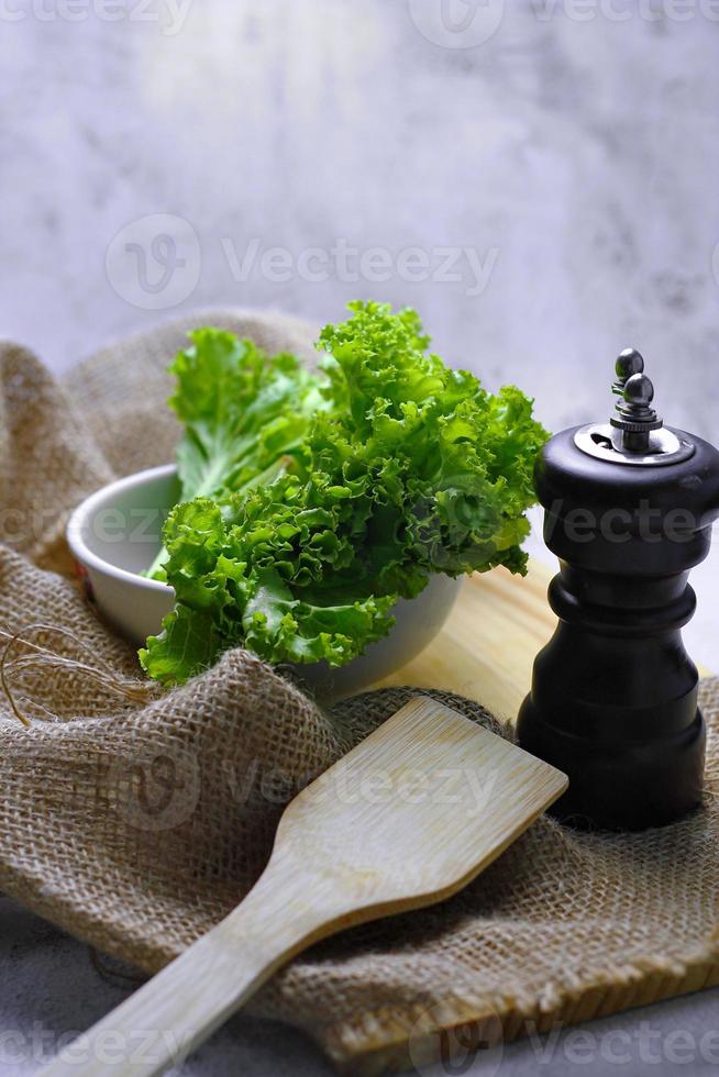 sla geplaatst in een wit kom en een snijdend bord Aan een wit tafel. groente salade. vegetarisch voedsel. schoon voedsel. groen groenten. foto