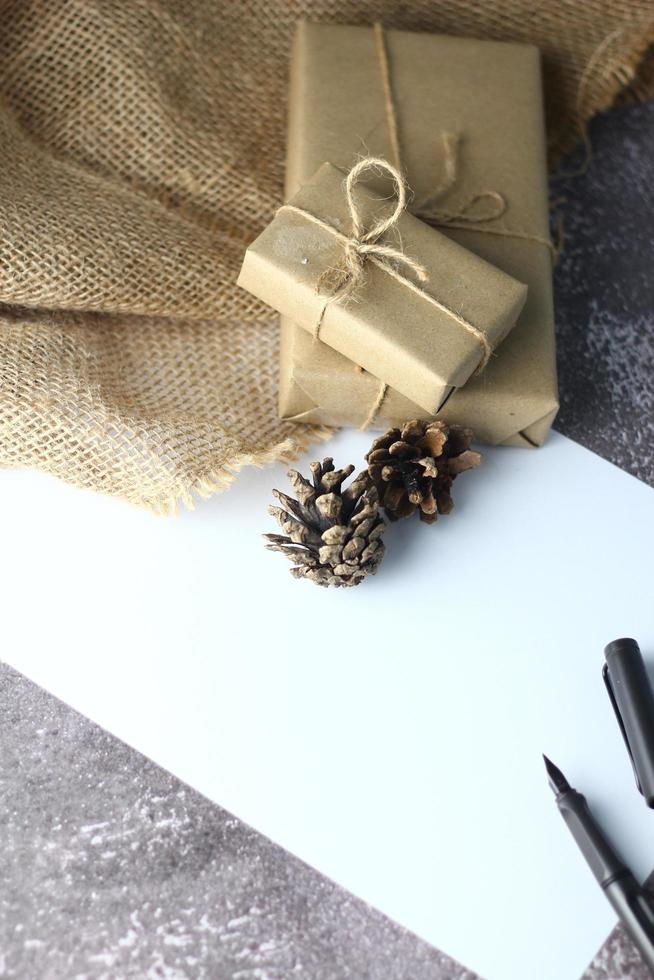 vakantie geschenken. Kerstmis en nieuw jaar.geschenk doos verpakt in bruin papier pijnboom kegels en wit papier en pennen geplaatst Aan de tafel, kopiëren ruimte. foto