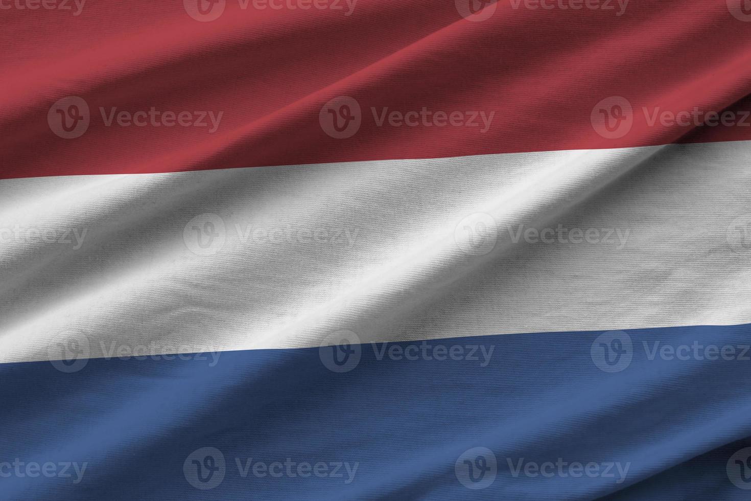 Nederland vlag met groot vouwen golvend dichtbij omhoog onder de studio licht binnenshuis. de officieel symbolen en kleuren in banier foto