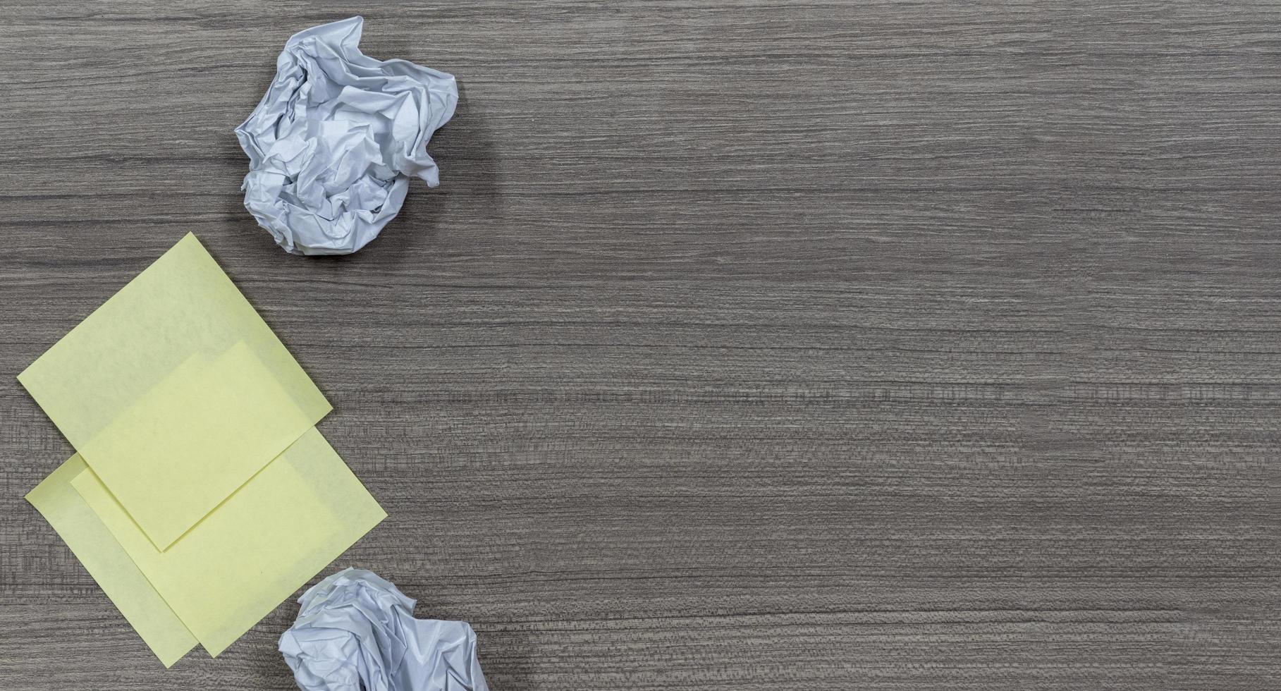 geel kleverig Notitie en verfrommeld papier bal Aan hout tafel met kopiëren ruimte foto