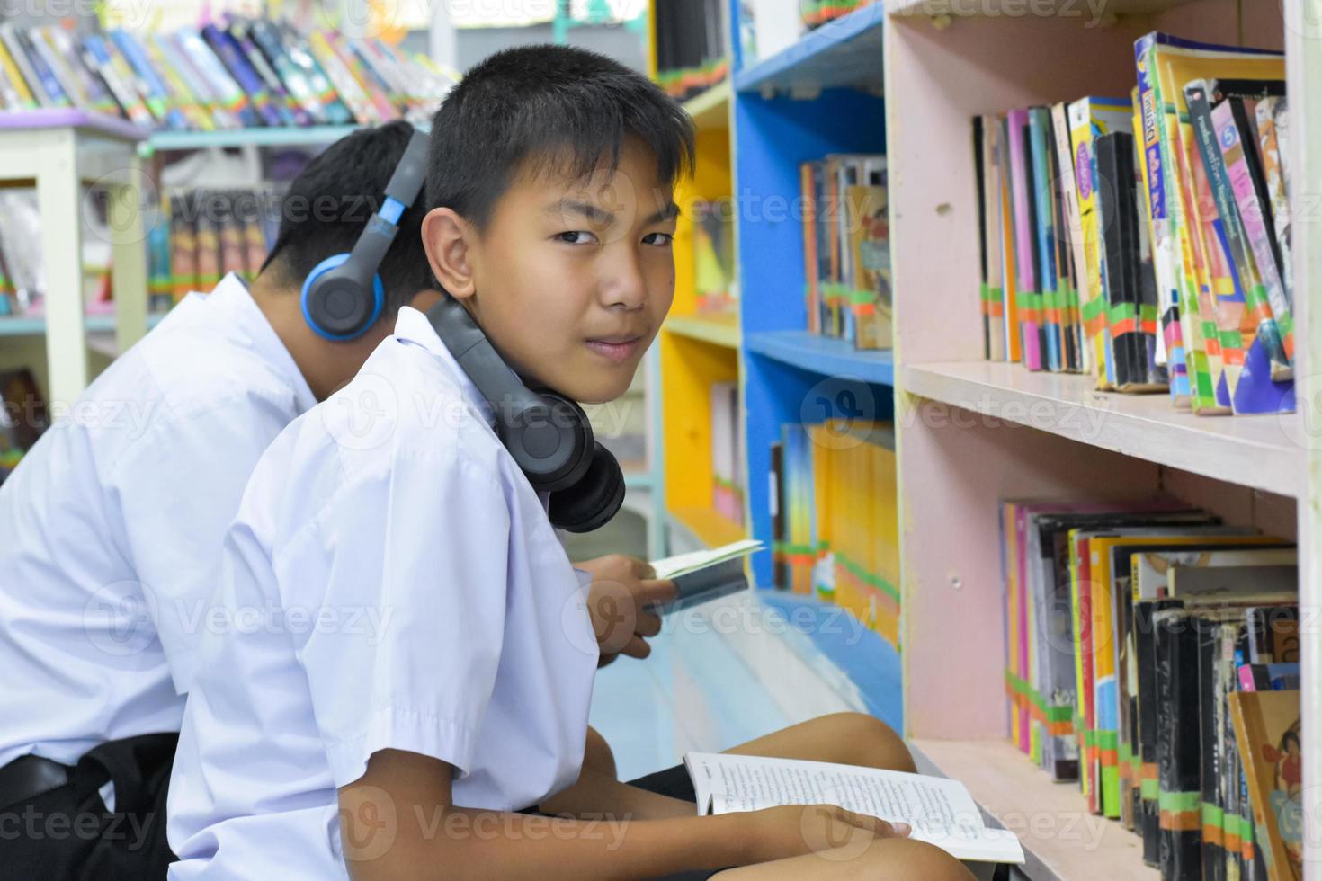 zacht fucus van twee Aziatisch jongen studenten zijn luisteren media, lezing en overleg plegen over favoriete boek Bij bibliotheek van school- foto