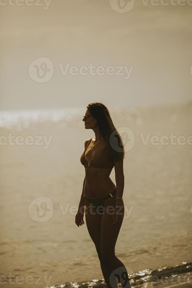 jong vrouw in bikini wandelen door de zee Aan een zonsondergang van zomer dag foto
