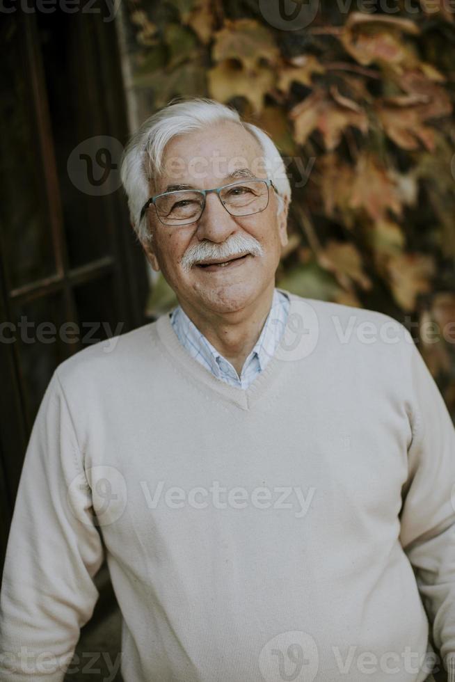 senior man die bij het raam staat op de herfstdag foto