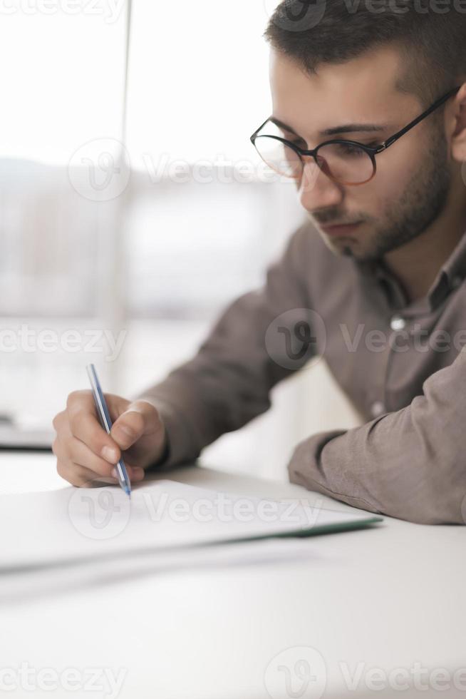 portret van jong Mens zittend Bij zijn bureau in de kantoor werken Aan is laptop foto