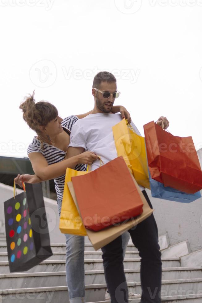 portret van vrolijk Kaukasisch jong paar Mens en vrouw Holding veel papier Tassen na boodschappen doen terwijl wandelen en pratend Aan straat. gelukkig familie paar met pakketjes buitenshuis. buying concept foto