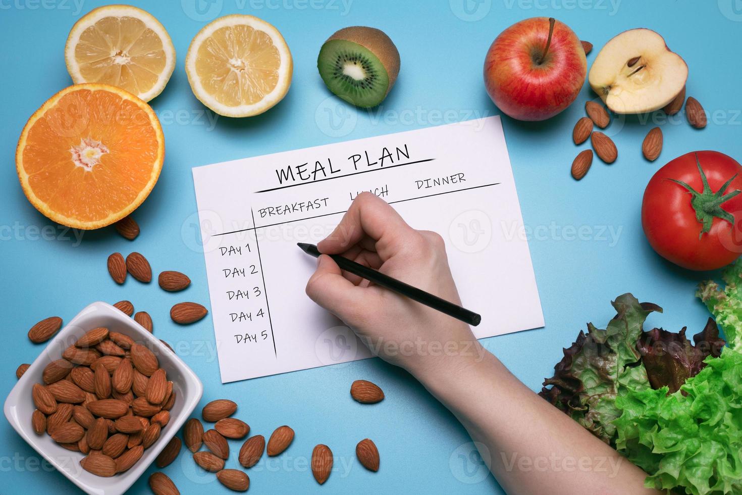 calorieën controle, maaltijd plan, eetpatroon en gewicht verlies concept. top visie van hand- vulling maaltijd plan. vlak leggen met divers fruit, groenten en noten Aan de blauw achtergrond. gezond voedsel foto