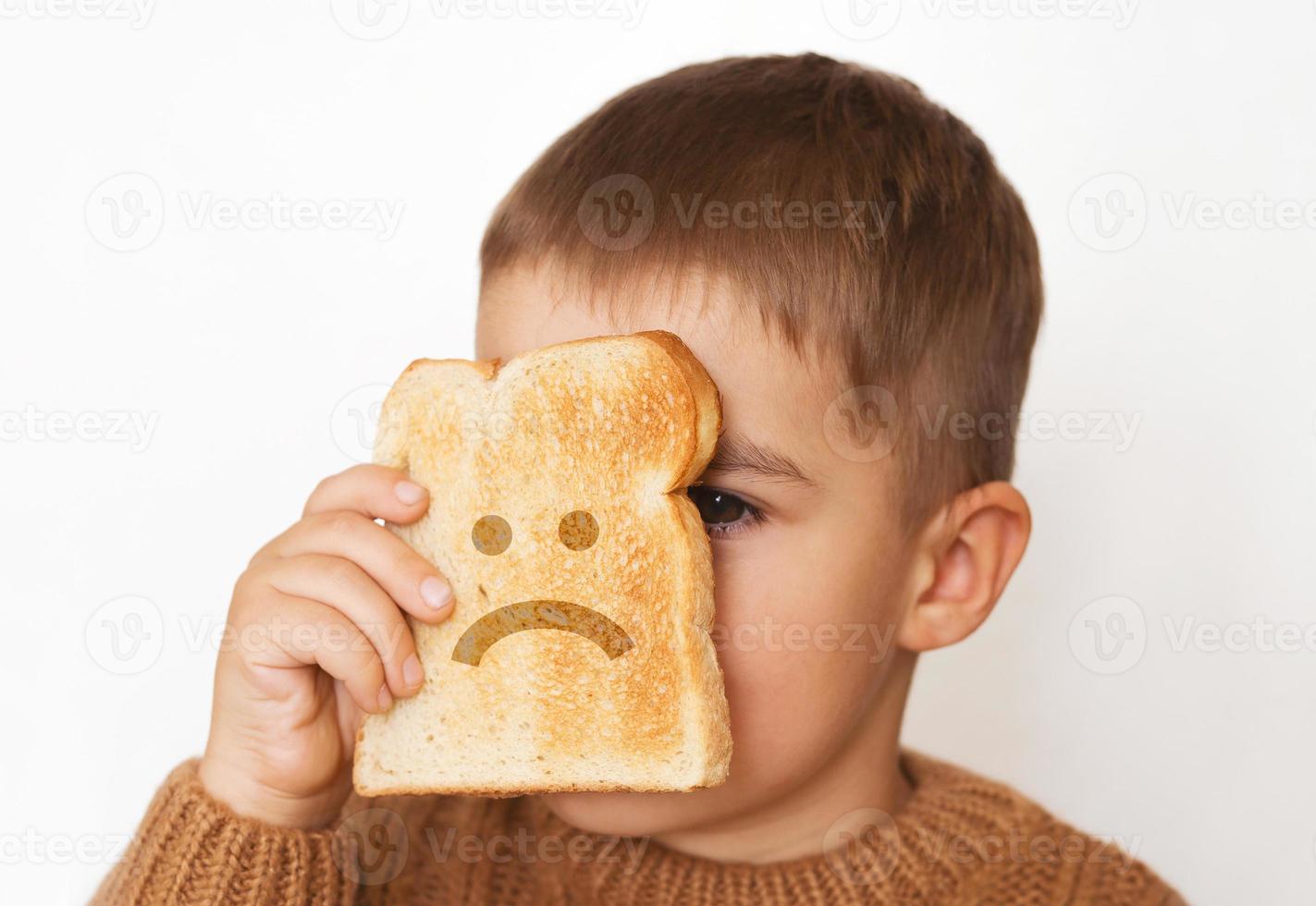 kinderen en gluten. peuter- jongen met geroosterd brood, met verdrietig emoji. gluten onverdraagzaamheid door kinderen. foto