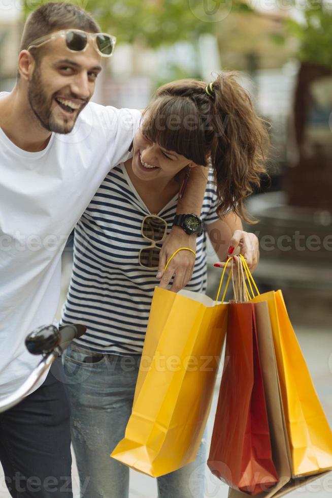 portret van vrolijk Kaukasisch jong paar Mens en vrouw Holding veel papier Tassen na boodschappen doen terwijl wandelen en pratend Aan straat. gelukkig familie paar met pakketjes buitenshuis. buying concept foto