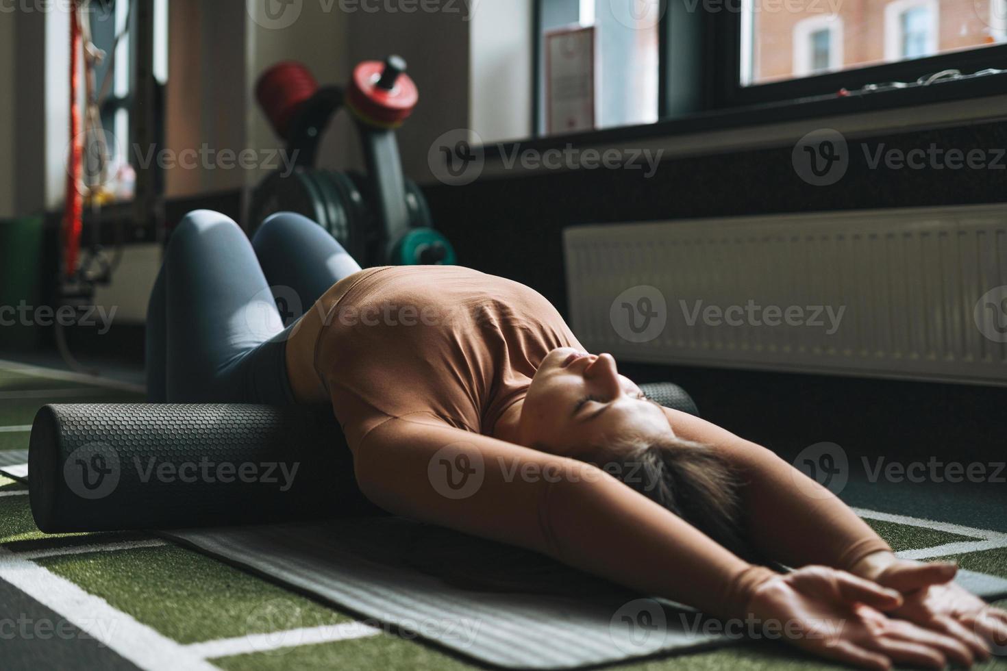 jong brunette vrouw aan het doen uitrekken pilates Aan massage rollen in geschiktheid club Sportschool foto