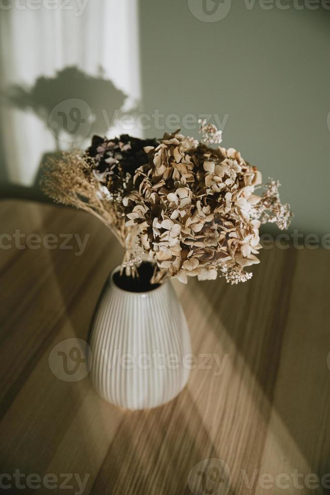 mooi boeket van droog bloemen in roze keramisch vaas Aan houten tafel in middag licht met wit muur in achtergrond foto