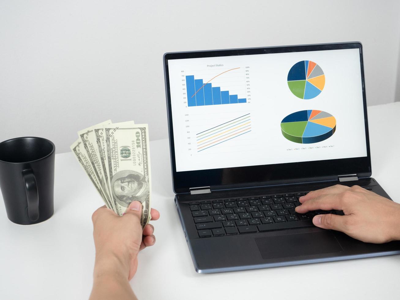 Mens hand- Holding geld dollar en gebruik makend van laptop Aan de tafel met koffie kop foto