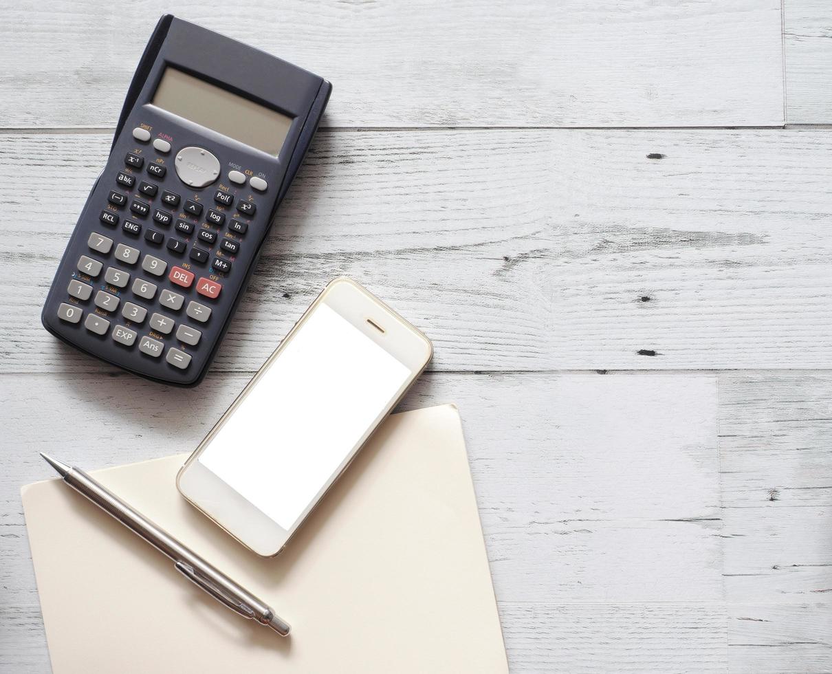 smartphone wit scherm zilver pen Aan blanco bladzijde notitieboekje met rekenmachine Aan wit hout tafel top visie en kopiëren ruimte foto