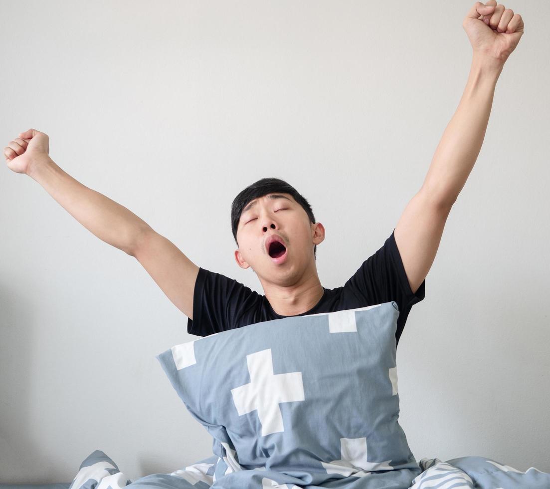 Aziatisch Mens met hoofdkussen wakker worden omhoog Bij ochtend- en arm omhoog en geeuw voelen slaperig Aan wit geïsoleerd foto