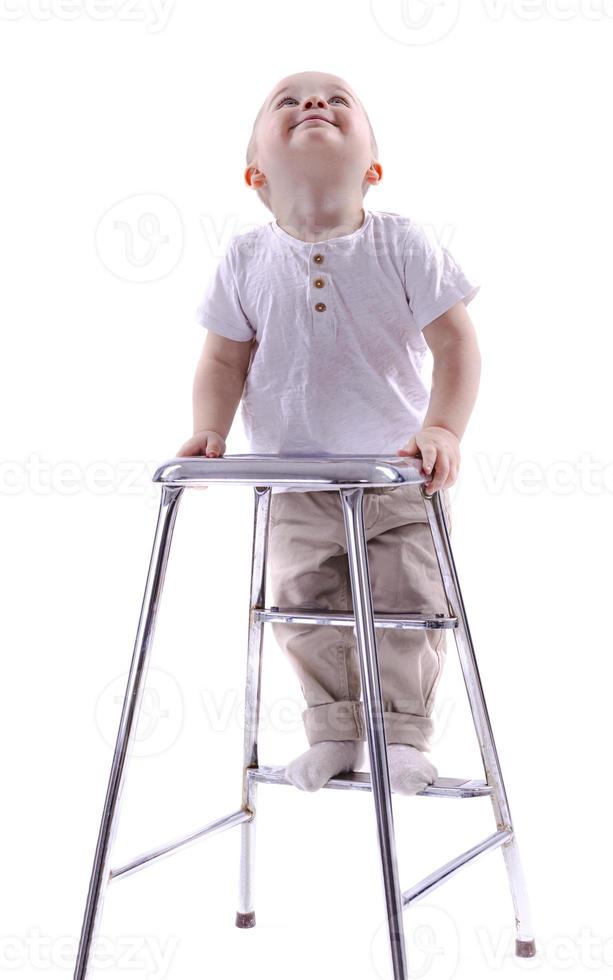 weinig jongen klimt op een ladder stoel. de begin van een carrière concept. grappig weinig jongen geïsoleerd Aan wit achtergrond. foto
