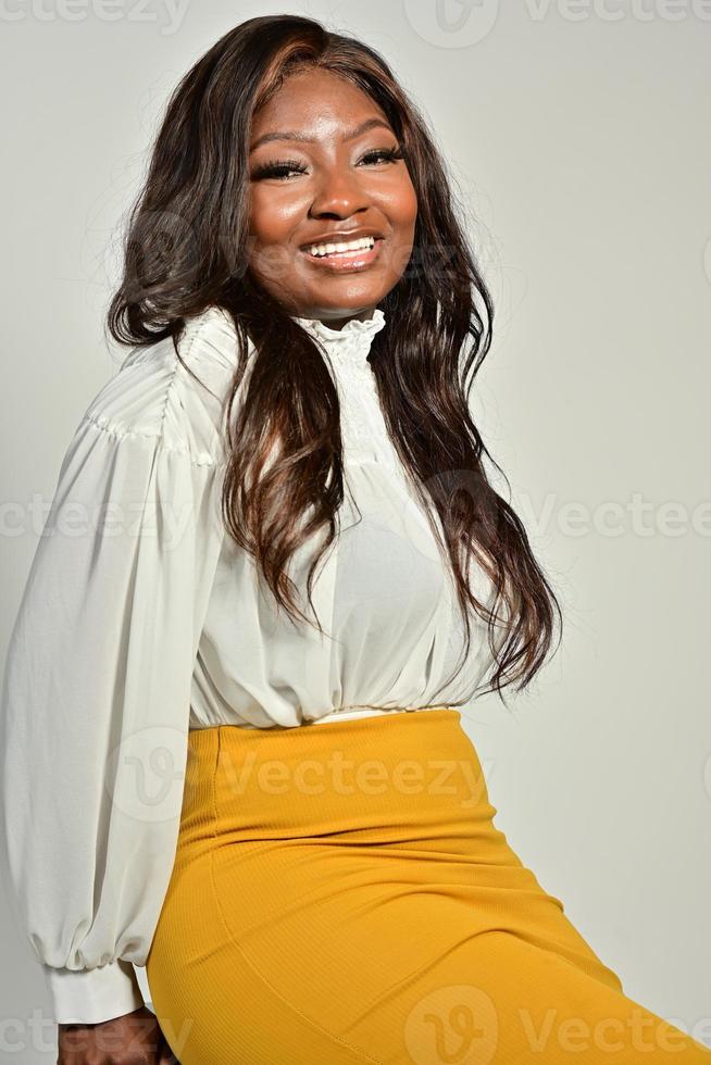 portret van mooi positief Afrikaanse Amerikaans vrouw in geel rok en wit overhemd staand en poseren in studio foto