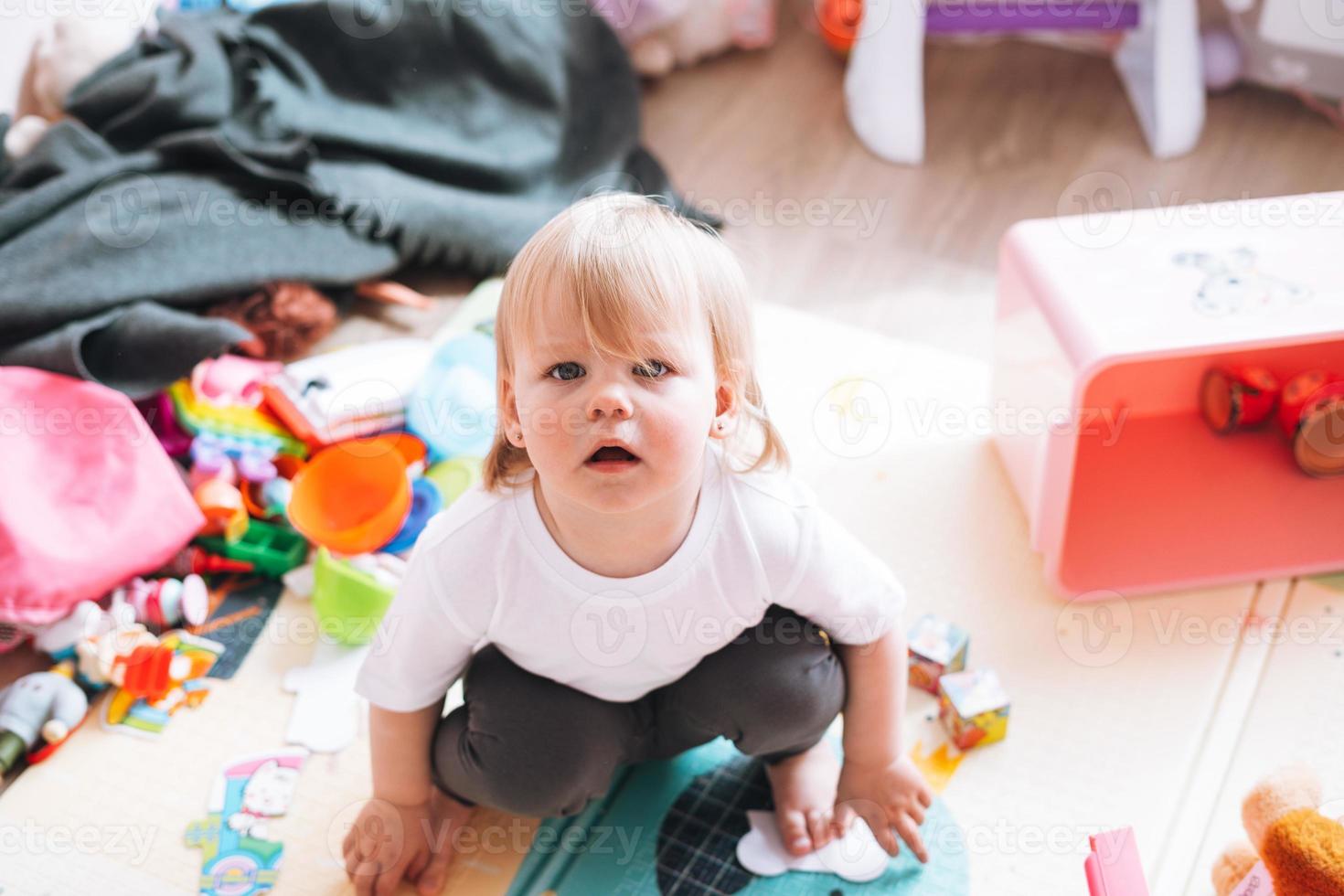 schattig grappig baby meisje zittend Aan verdieping in kinderen kamer Bij huis foto