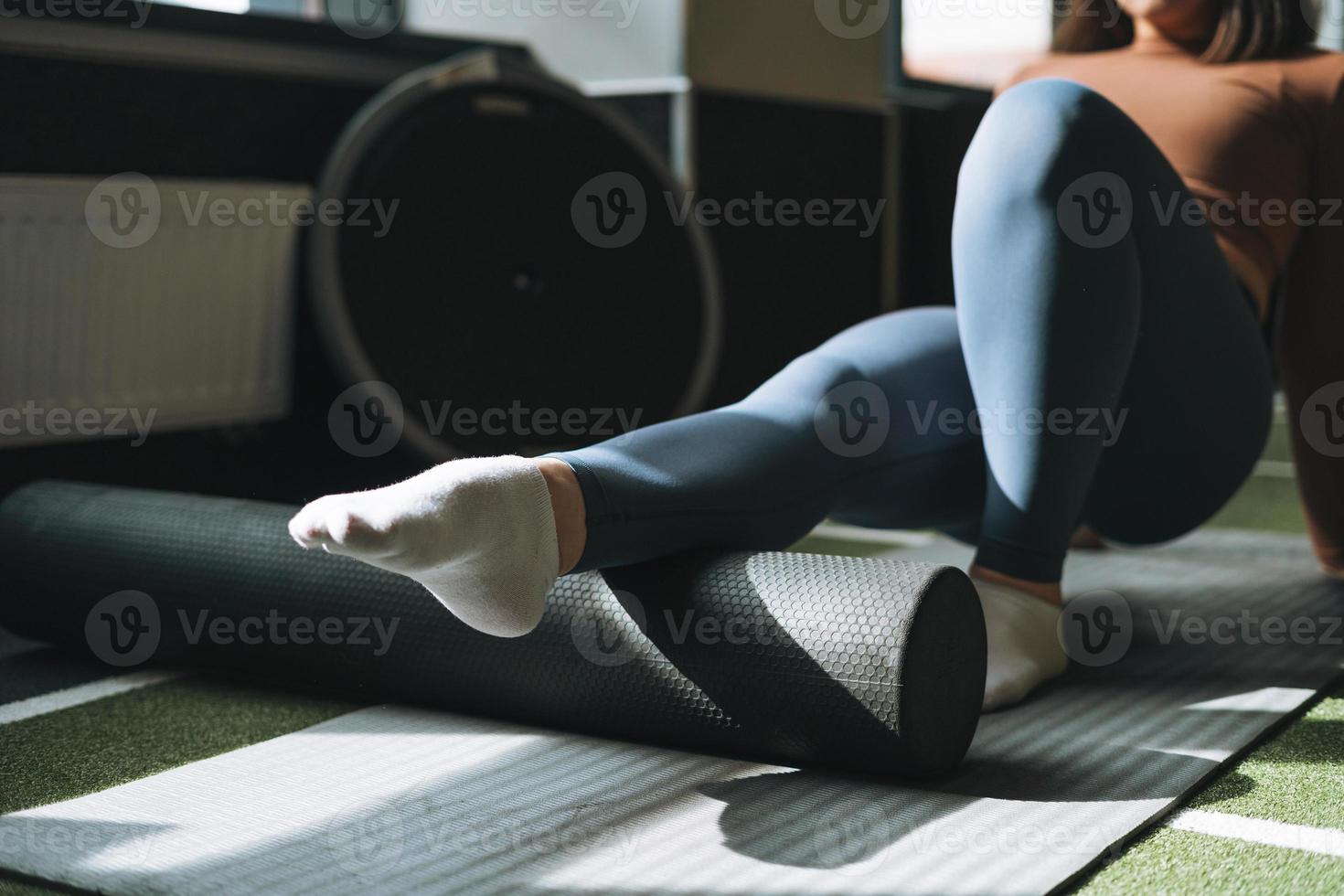 jong brunette vrouw aan het doen uitrekken pilates Aan massage rollen in geschiktheid club Sportschool foto