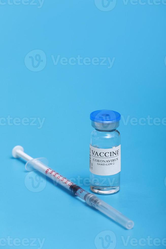 medicijnfles met coronavirusvaccin covid-19. medische glazen injectieflacon en spuit voor vaccinatie. vloeibaar vaccin in laboratorium, ziekenhuis of apotheek concept geïsoleerd op blauwe achtergrond foto