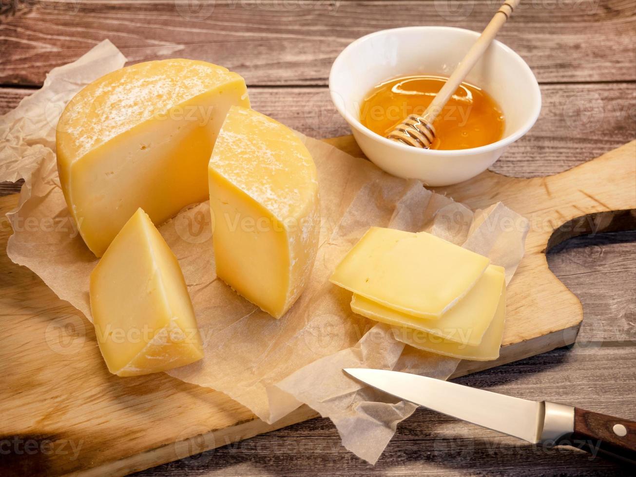 handgemaakt moeilijk kaas. natuurlijk boerderij kaas Aan een oud houten bord met honing in een kop foto