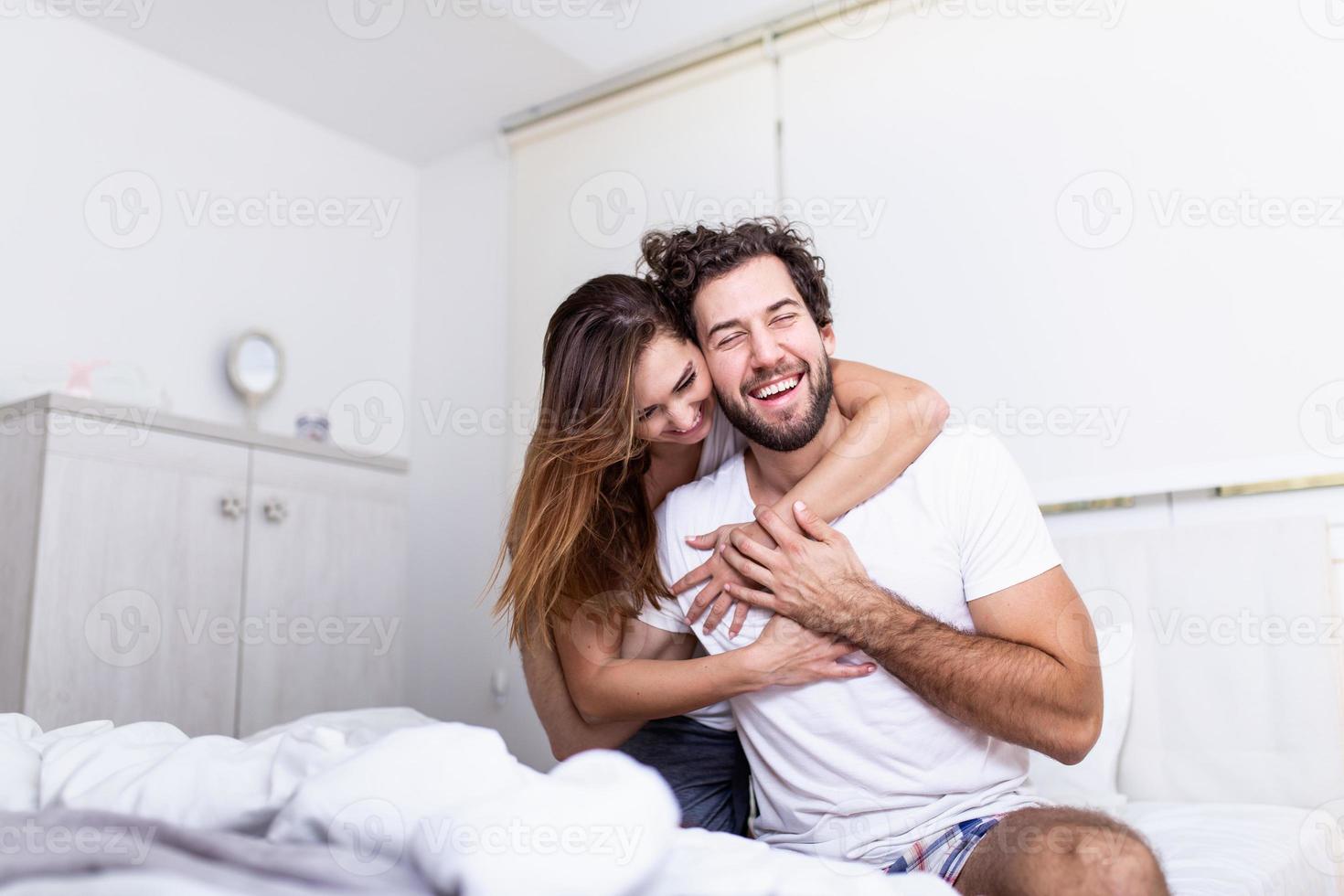 vrouw omarmen haar partner in bed, gelukkig paar in bed tonen emoties en liefde. mooi liefhebbend paar zoenen in bed. mooi jong paar aan het liegen samen Aan de bed. foto