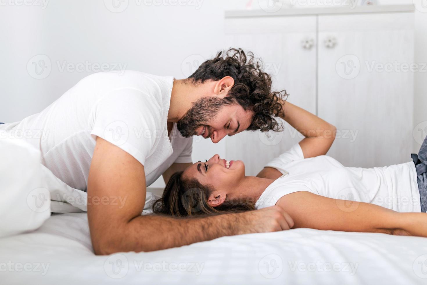 aanhankelijk jong aantrekkelijk paar sharing een romantisch moment in de slaapkamer Bij huis. gelukkig jong paar knuffelen en glimlachen terwijl aan het liegen Aan de bed in een slaapkamer Bij huis. foto