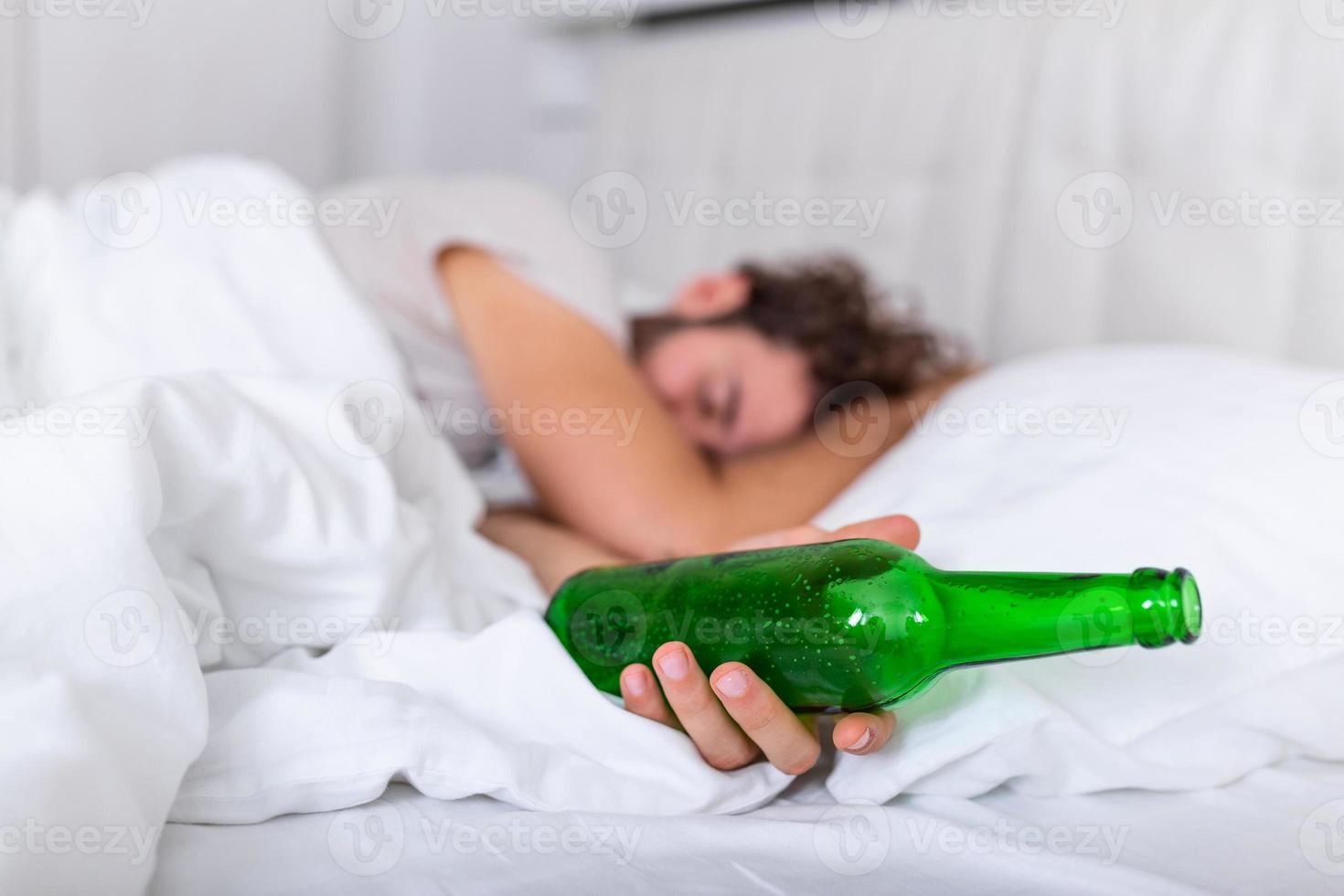 bewusteloos dronken Mens met fles van alcohol in handen slapen in bed . alcoholisme probleem en kater concept foto