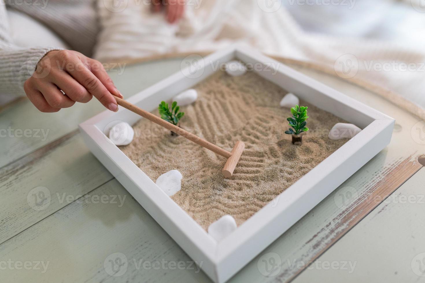 hand- van mooi jong vrouw gebruik makend van haar zen tuin Bij huis. lief jong glimlachen vrouw ontspannende met haar zen tuin en genieten van haar dag foto