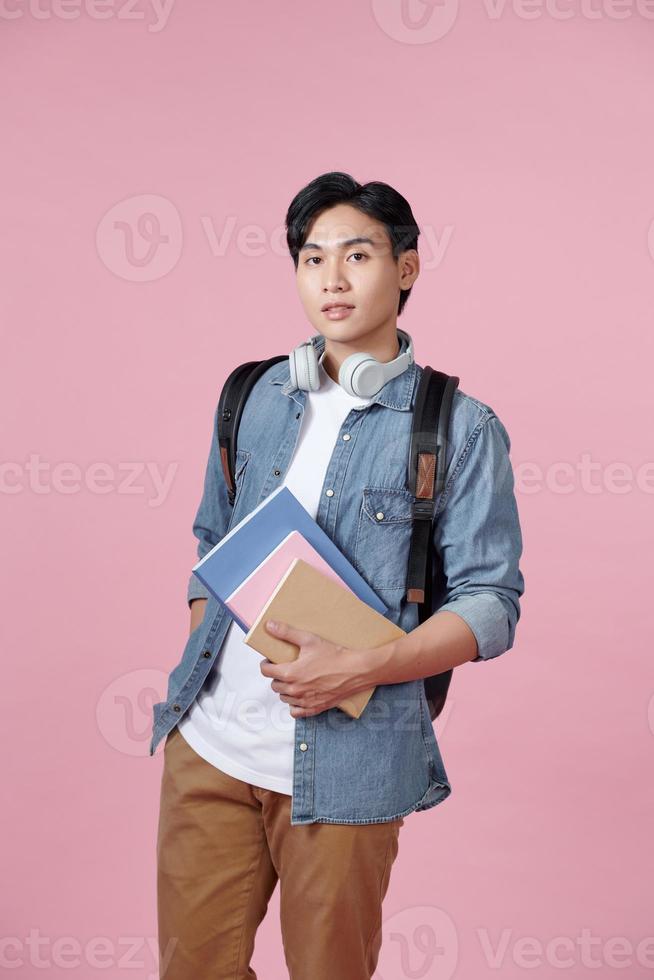 portret van glimlachen jong college leerling met boeken en rugzak tegen roze achtergrond foto