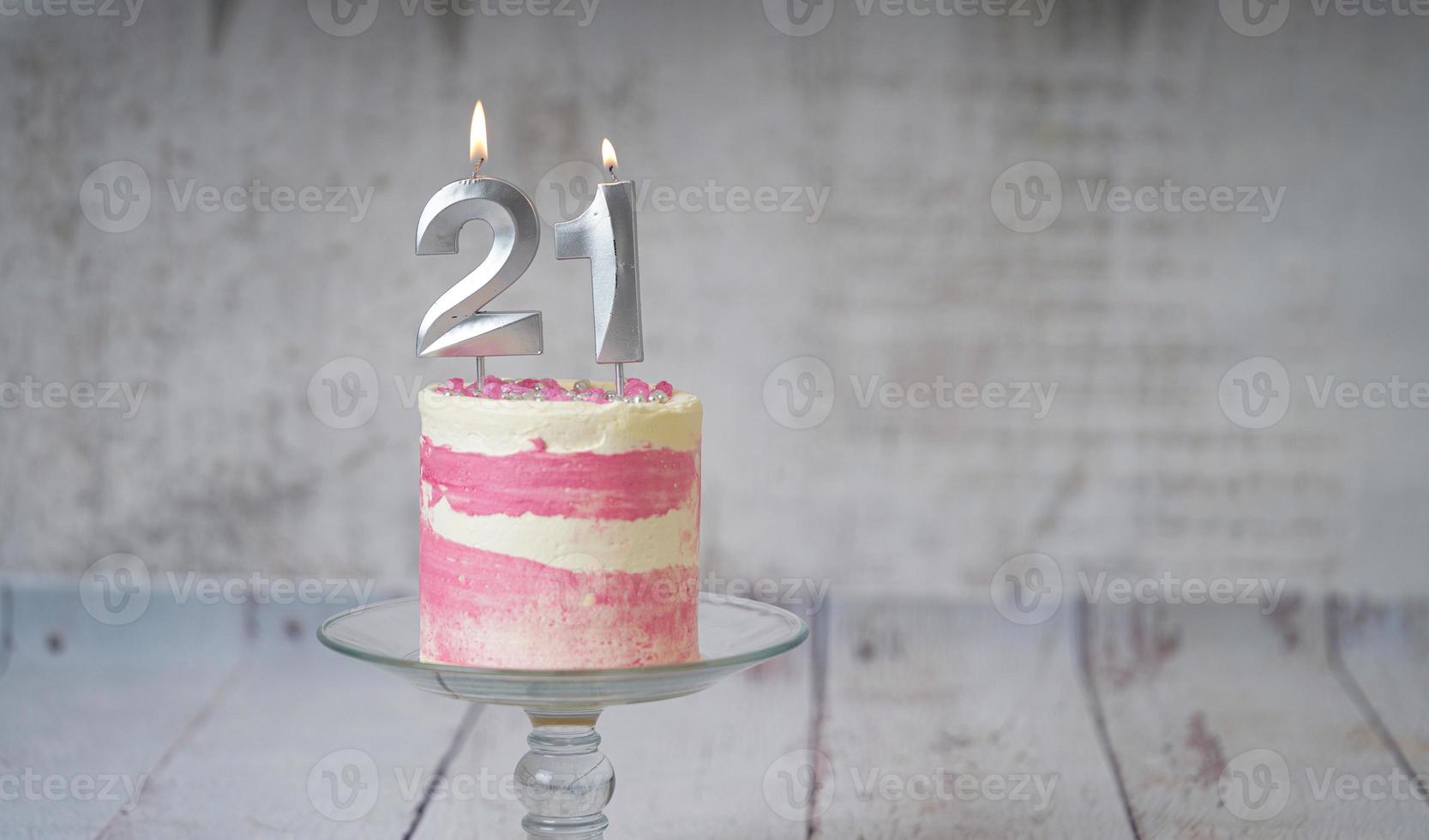 21e verjaardag taart roze en zilver taart met sommige hagelslag en 21e kaarslicht Aan een wit houten achtergrond. foto