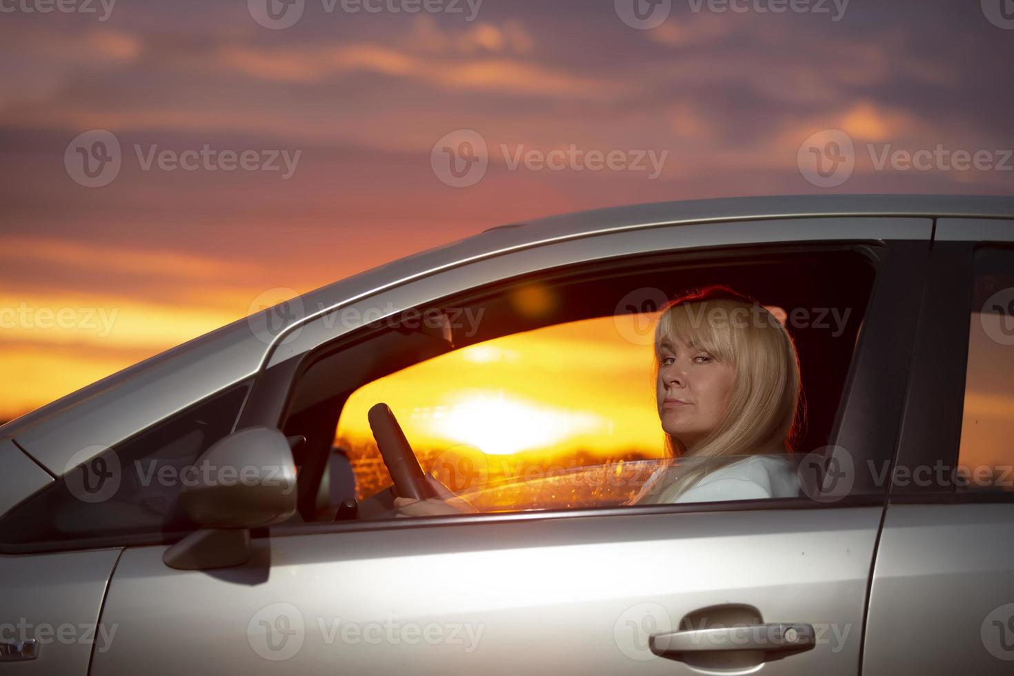 middelbare leeftijd vrouw het rijden een auto tegen de zonsondergang sky.vreemdeling foto