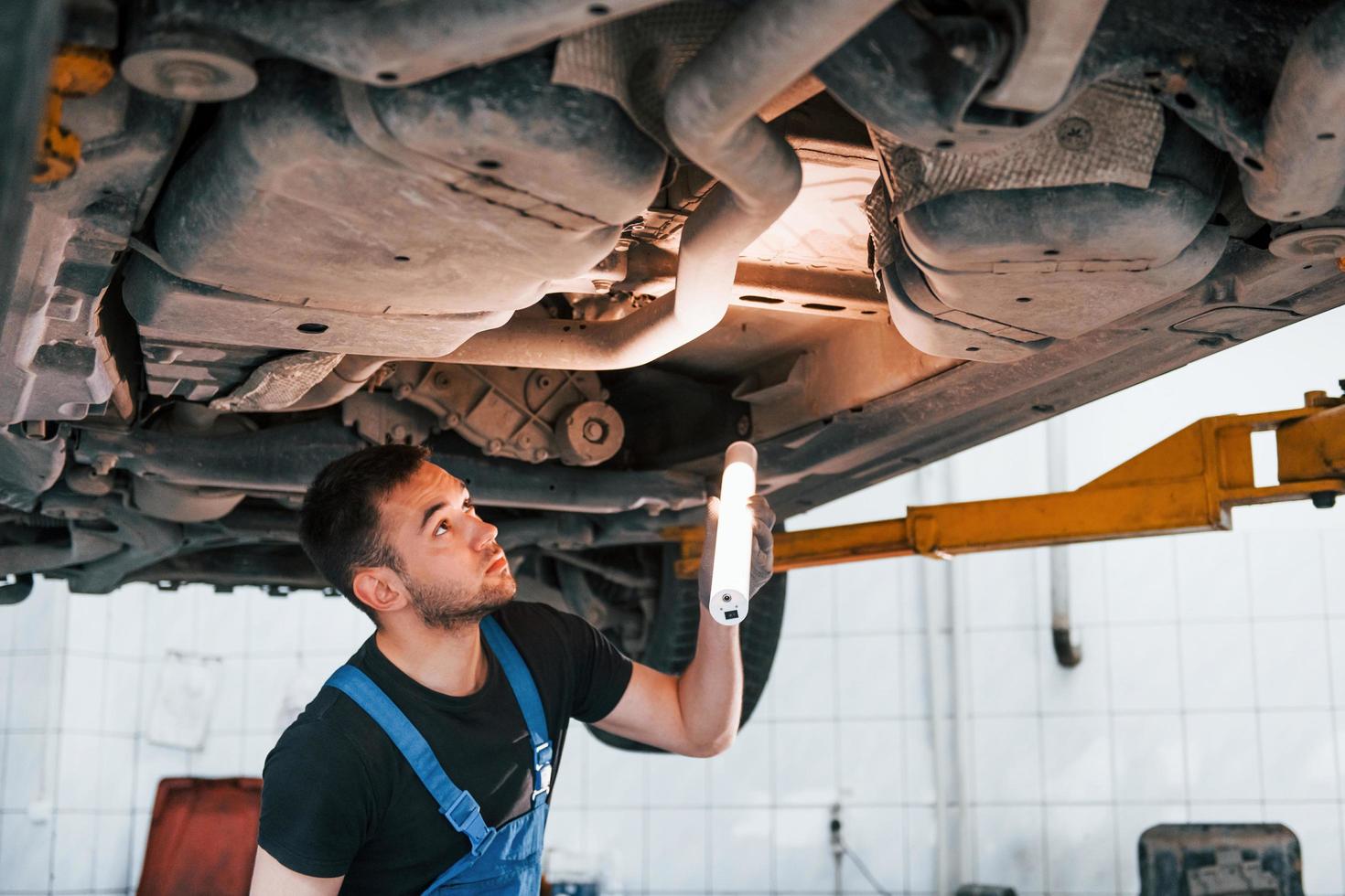 toepassingen verlichting apparatuur. Mens in werk uniform reparaties wit auto- binnenshuis. opvatting van auto- onderhoud foto