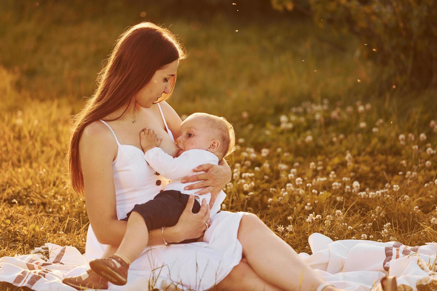 gelukkig moeder borstvoeding geeft haar zoon Aan de veld- Bij zonnig dag tijd van zomer foto
