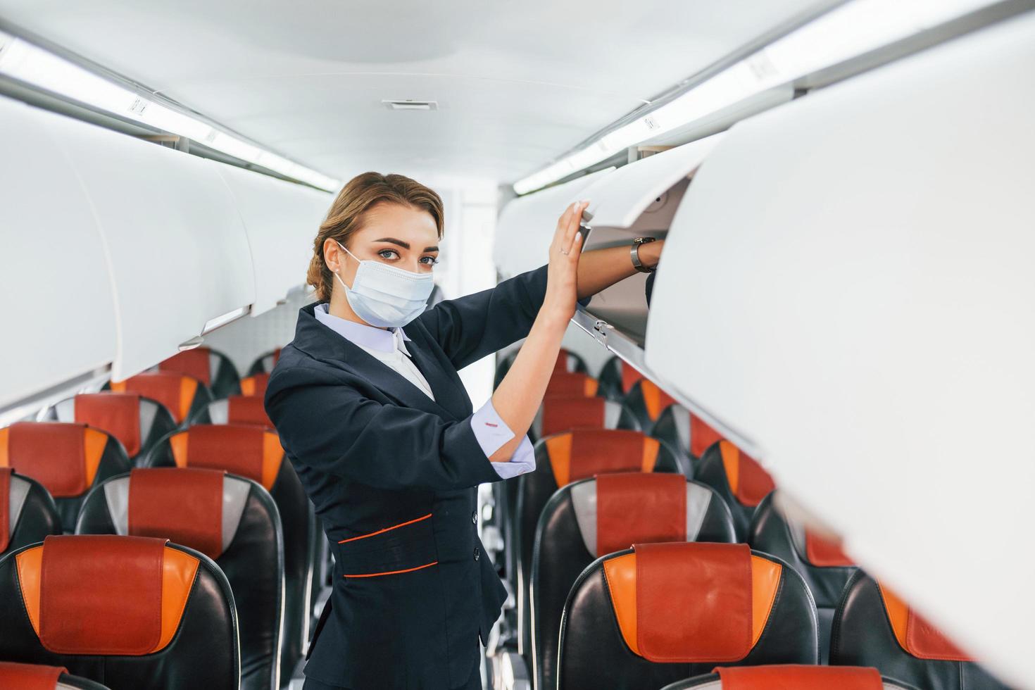 in masker. jong stewardess Aan de werk in de passagier vliegtuig foto